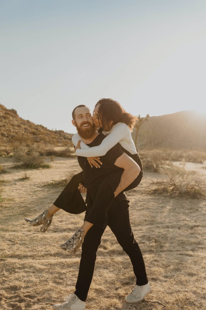 Young women jumping on man with beard's back. Happy couple smiling and in love 